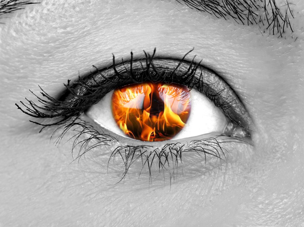 Close-up of an eye with an orange flame reflected in the iris, set against a black and white background.